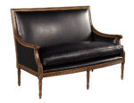 Compact black leather settee featuring a carved wood frame, high backrest, and nailhead trim for traditional interiors.