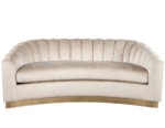 Curved beige velvet sofa with channel tufted backrest and an elegant brass-finished base for formal seating areas.