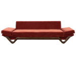Mid-century modern red velvet sofa with sloped arms and a sculpted wood base offering retro appeal and visual interest.